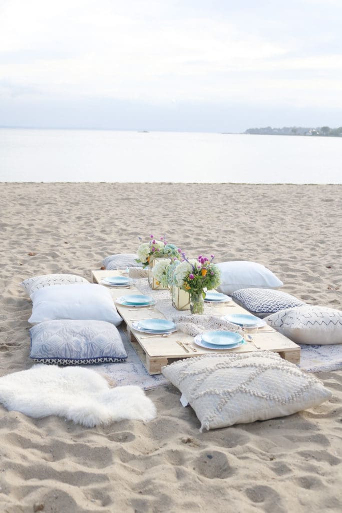 Boho Birthday Beach dinner with pillows and vintage rugs. Set up plates and table decor on pallet and add pillows. Birthday Beach dinner idea, beach dinner casual || Darling Darleen