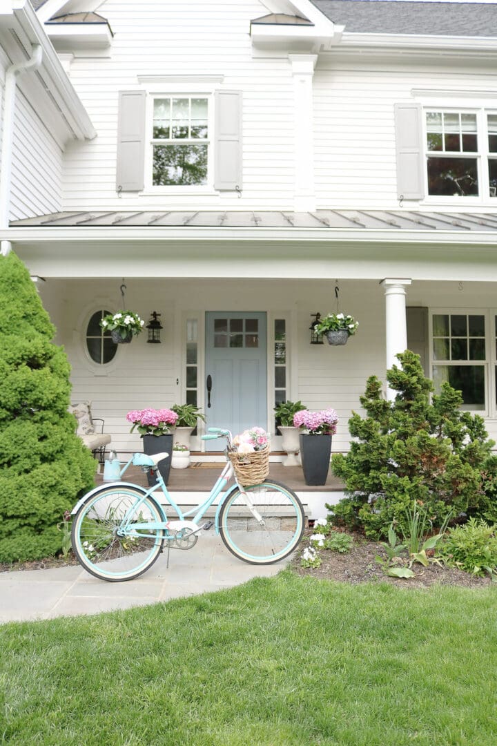 A beautiful home exterior can make or break curb appeal! Sharing 7 easy and simple curb appeal ideas || Darling Darleen Top CT Lifestyle Blogger home exterior | outdoor charm | curb appeal ideas | home exterior ideas | white house with gray shutters | porch swing | shutter | new england charm | blue front door | beach bike | flowering pots front door #darlingdarleen