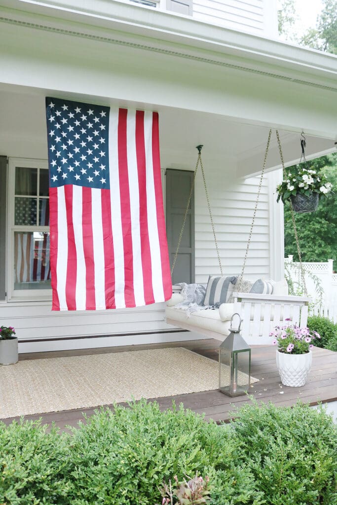 A beautiful home exterior can make or break curb appeal! Sharing 7 easy and simple curb appeal ideas . American flag on front porch. || Darling Darleen Top CT Lifestyle Blogger home exterior | outdoor charm | curb appeal ideas | home exterior ideas | white house with gray shutters | porch swing | shutter | new england charm | blue front door | #darlingdarleen