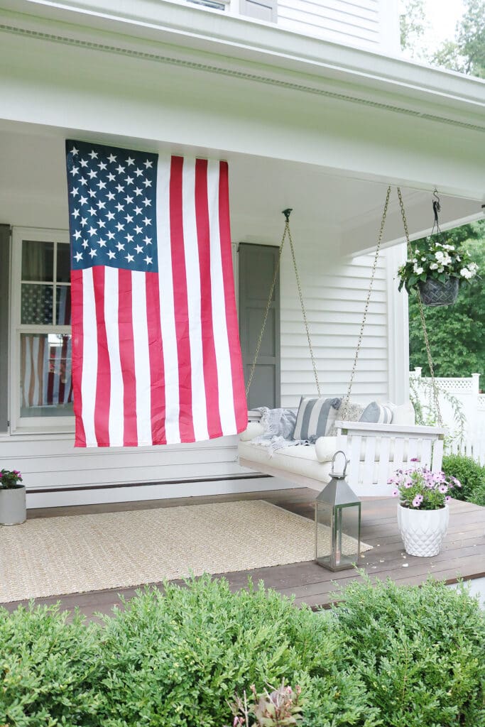 A beautiful home exterior can make or break curb appeal! Sharing 7 easy and simple curb appeal ideas . American flag on front porch. || Darling Darleen Top CT Lifestyle Blogger home exterior | outdoor charm | curb appeal ideas | home exterior ideas | white house with gray shutters | porch swing | shutter | new england charm | blue front door | #darlingdarleen