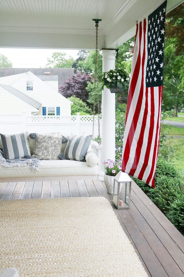 A beautiful home exterior can make or break curb appeal! Sharing 7 easy and simple curb appeal ideas. American flag by porch swing || Darling Darleen Top CT Lifestyle Blogger home exterior | outdoor charm | curb appeal ideas | home exterior ideas | white house with gray shutters | porch swing | shutter | new england charm | blue front door | #darlingdarleen